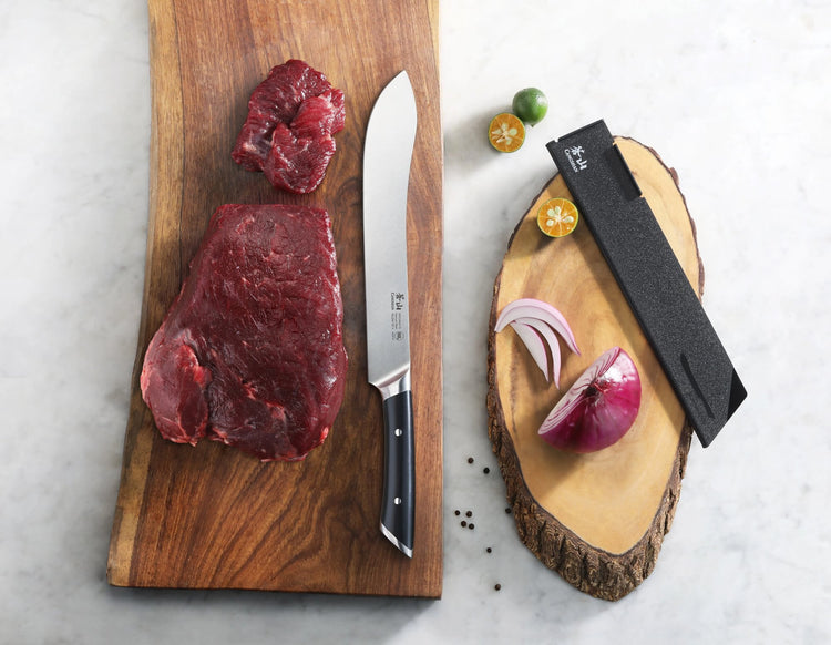 Butcher knife with black handle on wooden board next to raw beef, sliced onion, halved kumquats, and knife sheath.