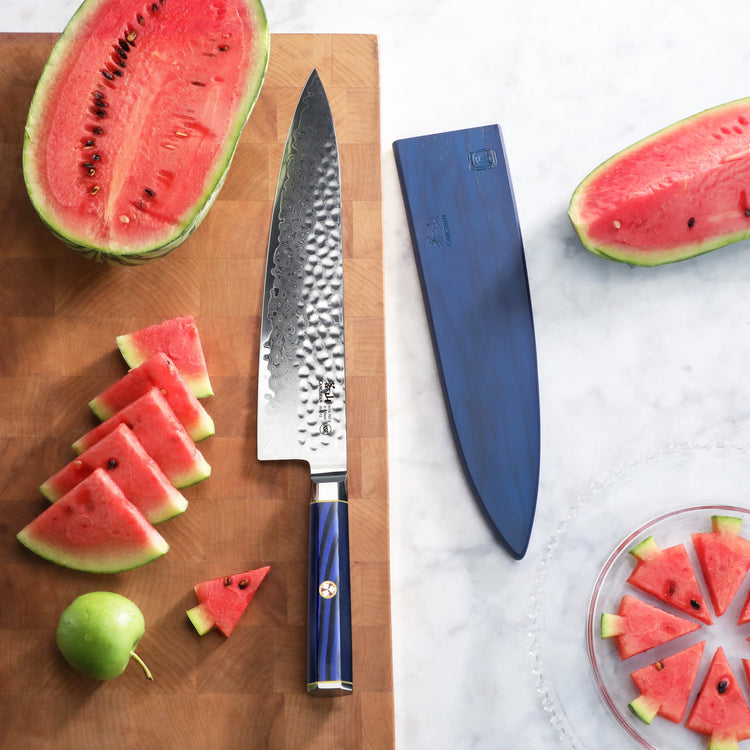 10-inch chef's knife with hammered Damascus steel blade and blue handle on cutting board with sliced watermelon and green app