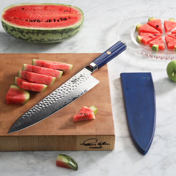 10-inch chef's knife with blue handle and hammered Damascus steel blade on wooden cutting board with sliced watermelon.