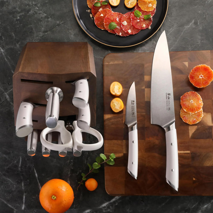 12-piece knife set with acacia wood block, two knives on cutting board with sliced citrus fruits.