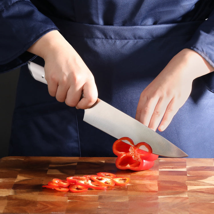 Person slicing a red bell pepper on a wooden cutting board with a large kitchen knife.