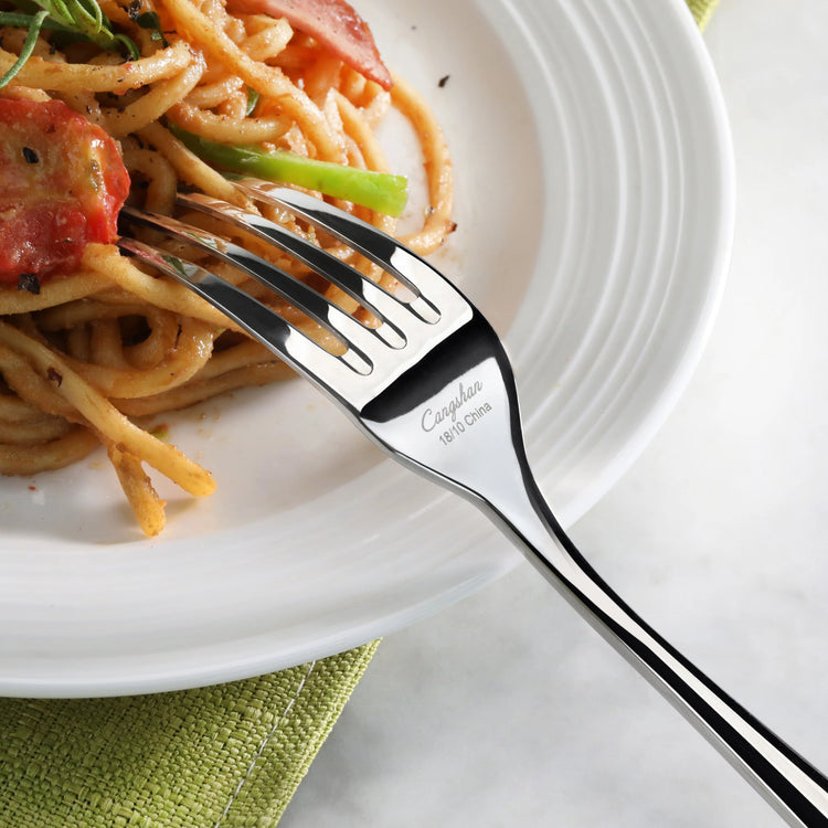 Fork resting on a white plate with spaghetti, tomato, and green vegetable on a green cloth.