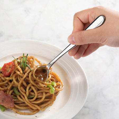 Hand holding a stainless steel fork twirling noodles with vegetables on a white plate.