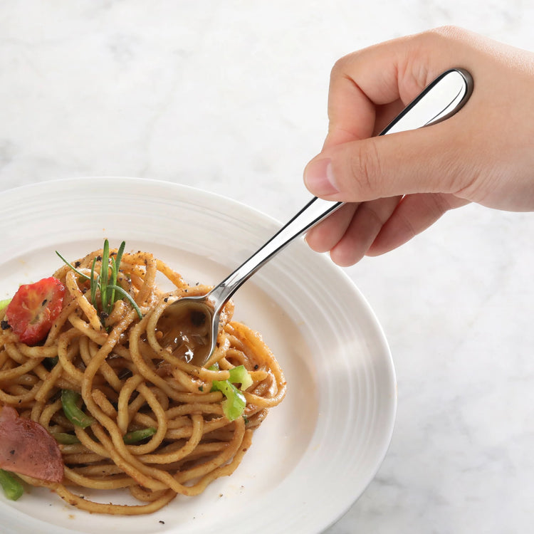 Hand holding a stainless steel fork twirling noodles with vegetables on a white plate.