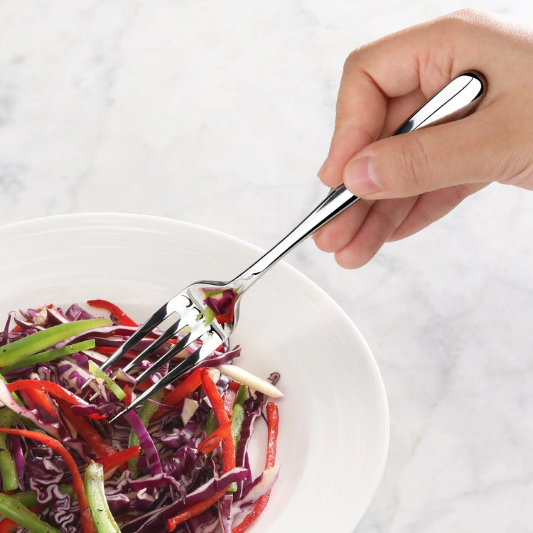 Hand holding a polished stainless steel salad fork spearing mixed sliced vegetables in a white bowl.