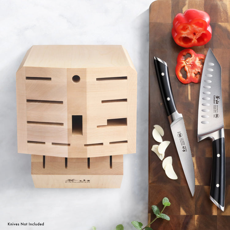 Empty maple knife block with 16 slots next to a cutting board holding two knives, sliced red bell pepper, and garlic cloves.