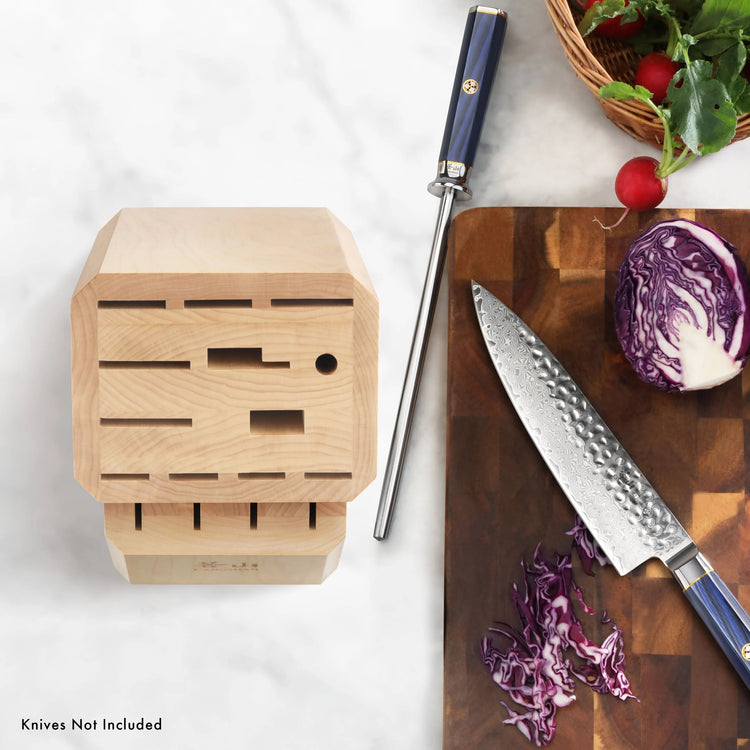 Empty 16-slot maple knife block with flat top next to a sharpening steel and a cutting board with a chef's knife and sliced p