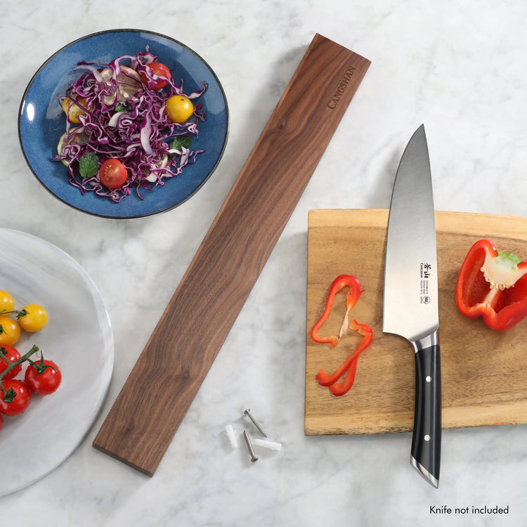 Walnut magnetic knife bar with mounting screws next to a cutting board, chef's knife, and sliced red bell pepper.