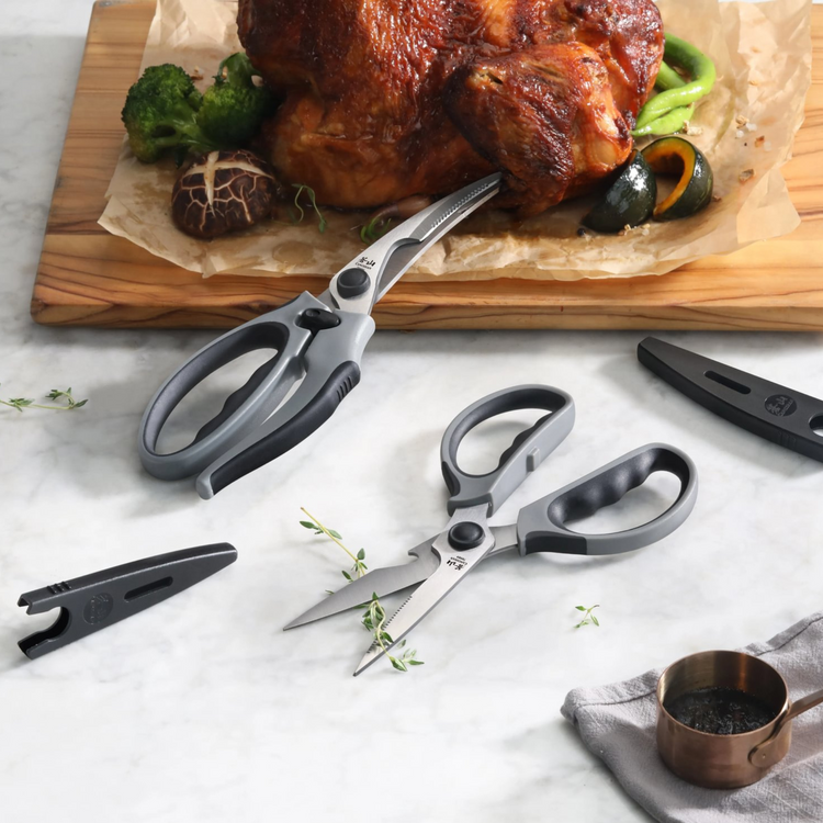 Gray 2-piece heavy-duty kitchen shears set with protective guards, one pair cutting roasted chicken on wooden board.