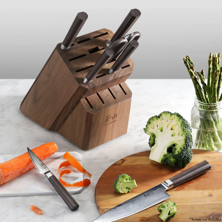 Wooden knife block with multiple slots, holding several knives, placed on a kitchen counter with vegetables nearby.