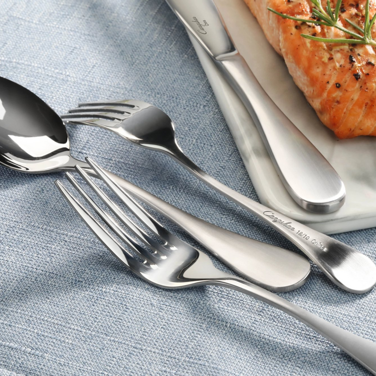 Stainless steel flatware with matte finish handles, including a bouillon spoon, fork, and knife on a blue cloth next to cooke