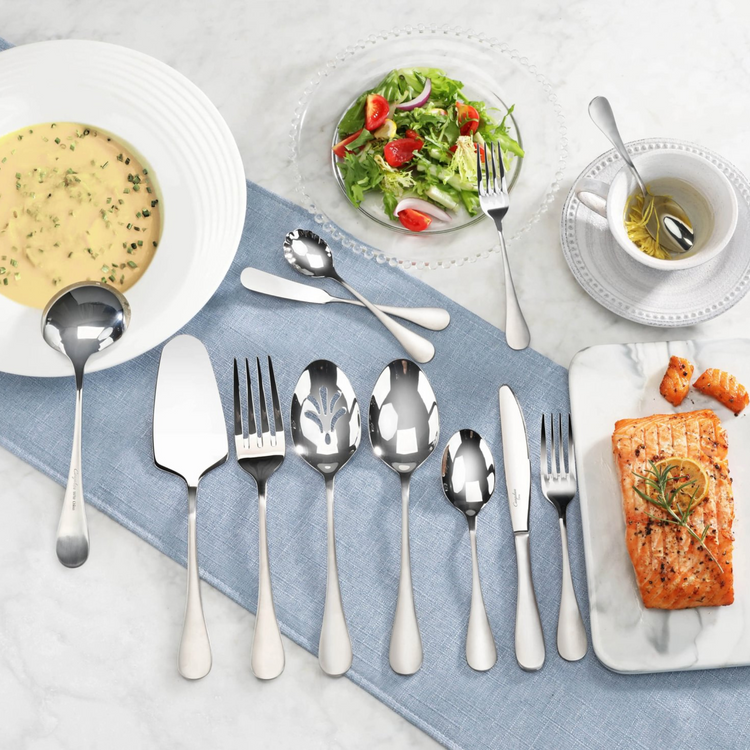 Set of stainless steel flatware with matte finish handles displayed on a blue cloth, alongside soup, salad, tea, and salmon.