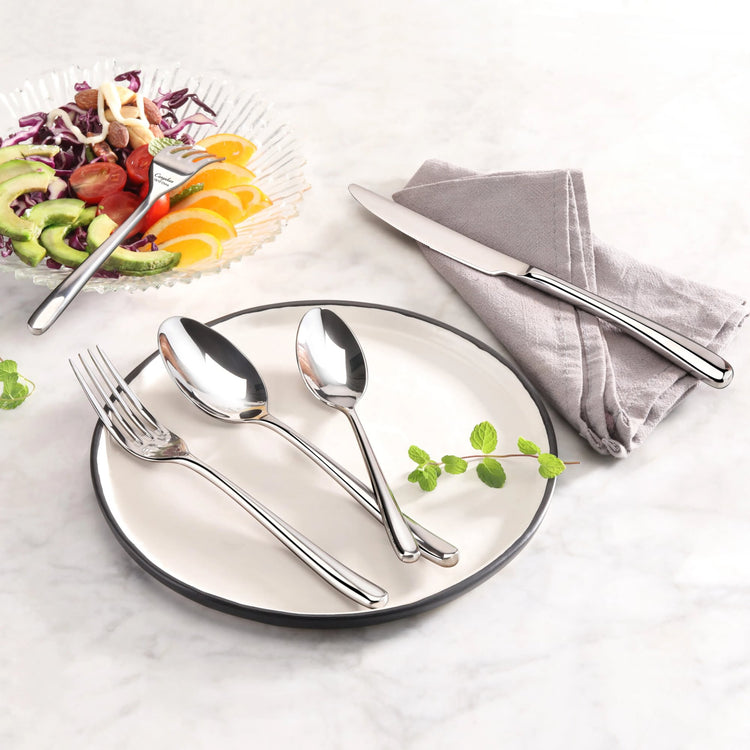 Fork, two spoons on a white plate with a green garnish, and a knife on a gray napkin on a marble surface.
