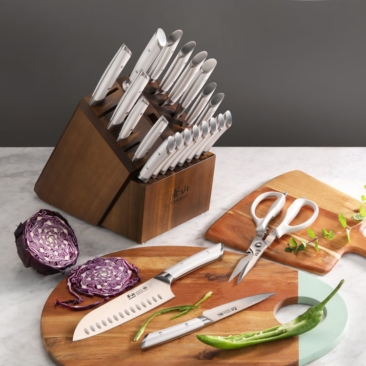 23-piece knife set with stainless steel blades in acacia wood block, displayed with kitchen scissors and vegetables.
