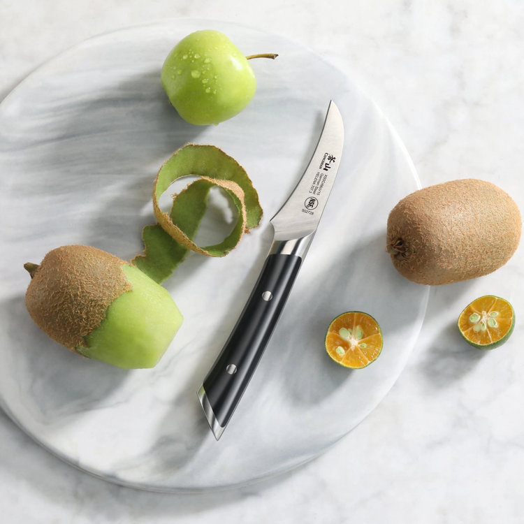 Peeling knife with black handle on a marble plate, partially peeled green apple, kiwi, and halved kumquats.