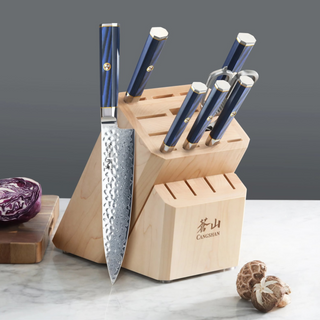 
                    
                      Knife block with six knives featuring blue handles, placed on a marble surface with mushrooms and a cutting board nearby.
                    
                  