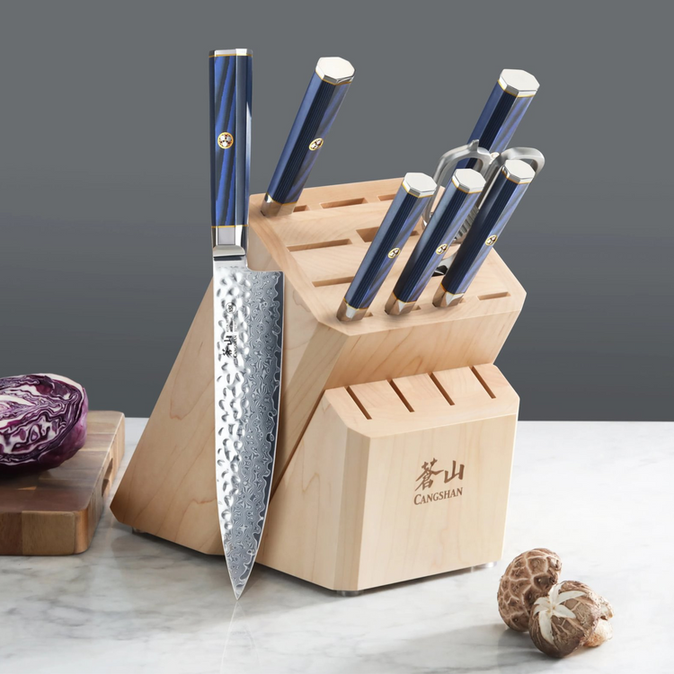 Knife block with six knives featuring blue handles, placed on a marble surface with mushrooms and a cutting board nearby.
