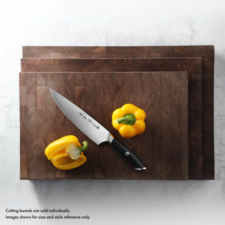 Three stacked walnut end-grain cutting boards with a chef's knife and two yellow bell peppers on the top board.