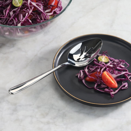 Slotted stainless steel serving spoon with mirror finish on a black plate with red cabbage and tomato slices.
