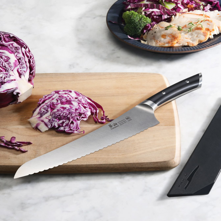 9-inch serrated deli knife with black handle on wooden cutting board next to sliced purple cabbage.