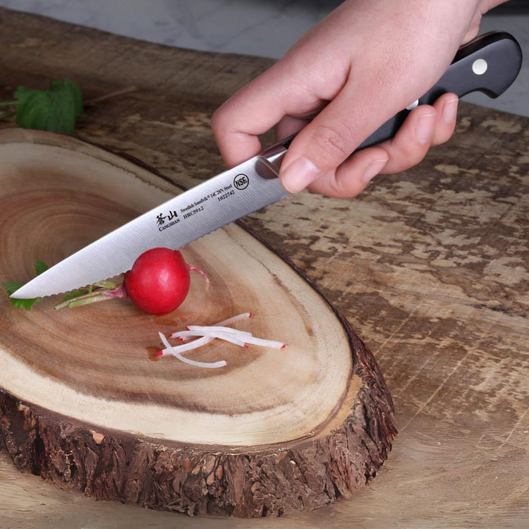 Hand holding a serrated knife slicing a radish on a wooden cutting board shaped like a tree slice.