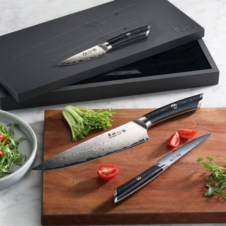 Three-piece knife set with patterned blades and dark handles, displayed with tomatoes and greens on a wooden board and in a b