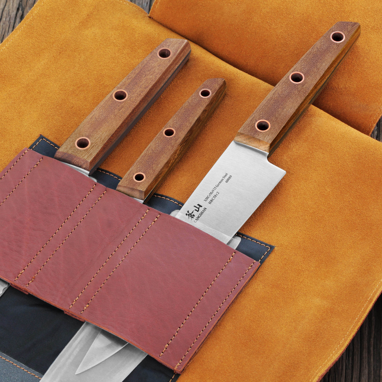 Four knives with wooden handles secured in stitched leather roll with tan suede interior on wooden surface