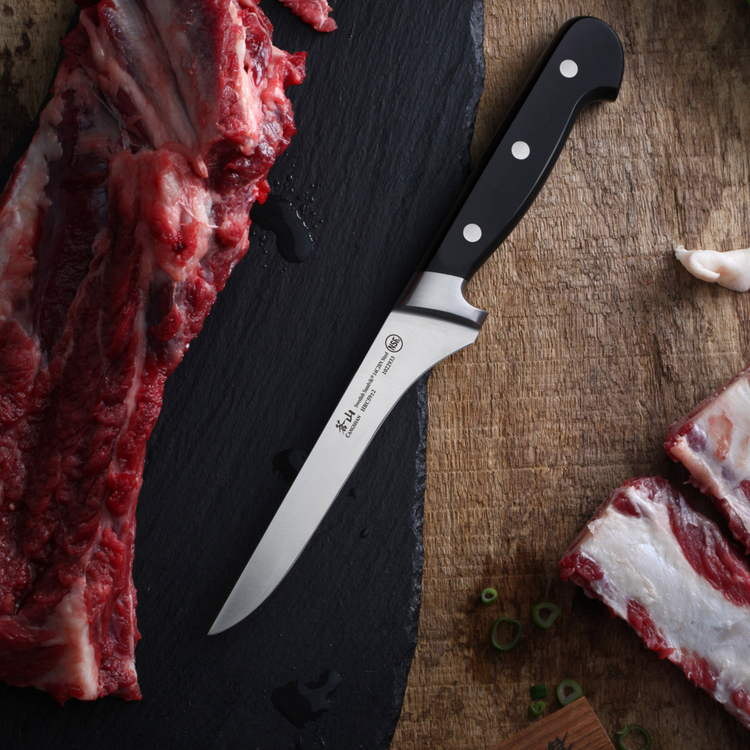 Butcher knife with a black handle placed between raw meat pieces on a wooden and slate surface.