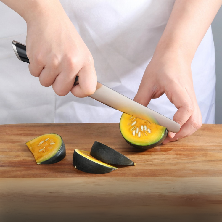 Hand holding a serrated utility knife slicing a small round squash on a wooden cutting board.