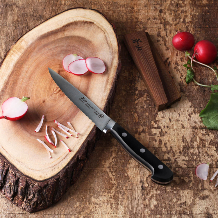 Serrated kitchen knife on a wooden cutting board with sliced radishes and whole radishes nearby.