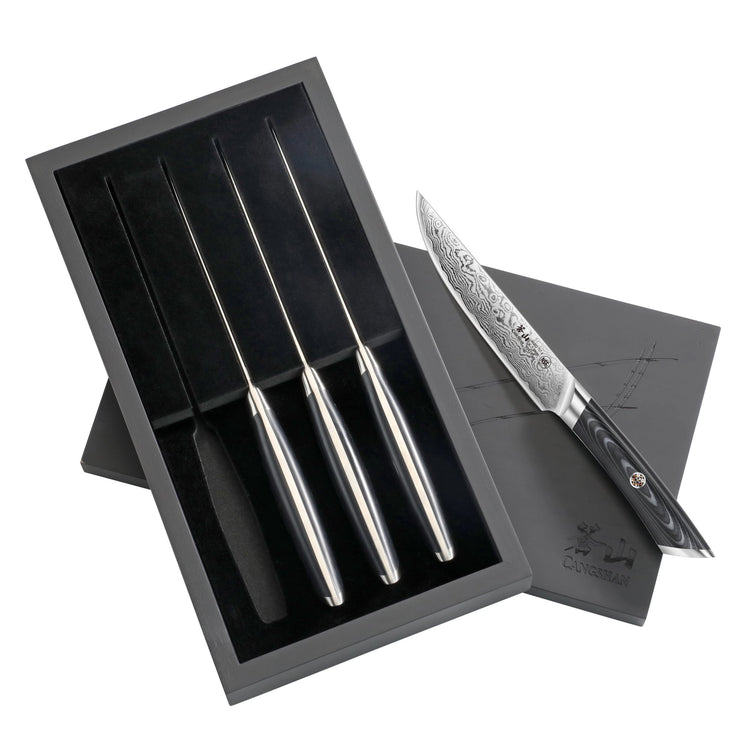 Four steak knives with patterned blades and polished handles in a black presentation box with lid.