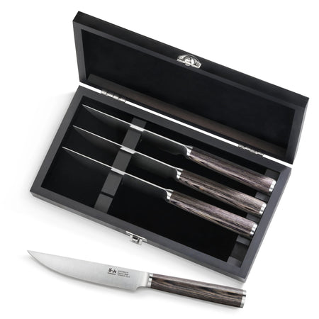 Four steak knives with pakkawood handles in a black wood box, one knife placed outside the box.