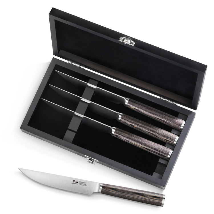 Four steak knives with pakkawood handles in a black wood box, one knife placed outside the box.