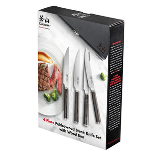 
                    
                      Four steak knives with pakkawood handles displayed next to sliced steak and broccoli, packaged in a black wood box.
                    
                  