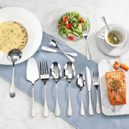 Set of stainless steel flatware with matte finish handles displayed on a blue cloth, alongside soup, salad, and salmon dishes