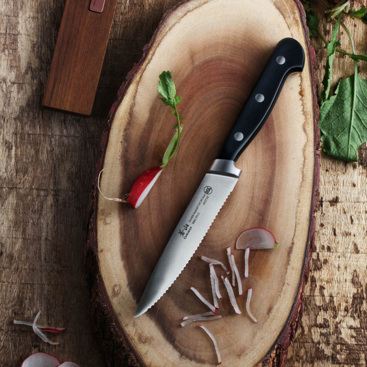 Serrated knife with black handle on wooden cutting board next to sliced radish and radish with leaf.