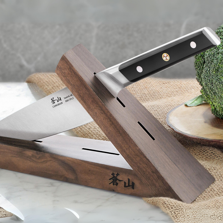 Walnut wood knife block holding a kitchen knife with a black handle, placed on a marble surface near broccoli.