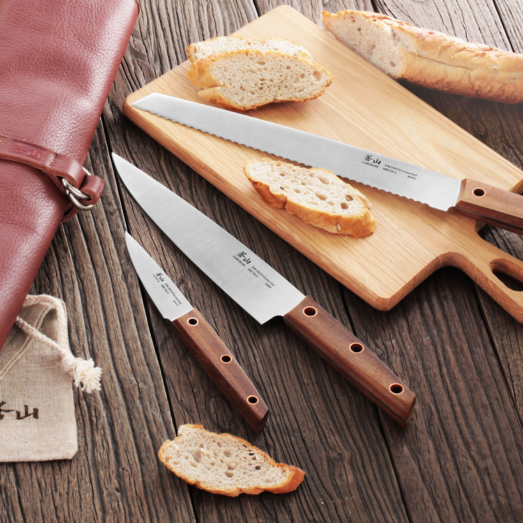 Three knives with wooden handles and German steel blades displayed on a wooden surface with sliced bread and a leather roll k