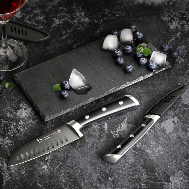 Two black-handled knives next to a slate board with blueberries, ice cubes, and small green leaves on a dark surface.