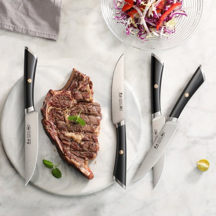 Four steak knives with black handles arranged around a cooked ribeye steak on a white marble surface.