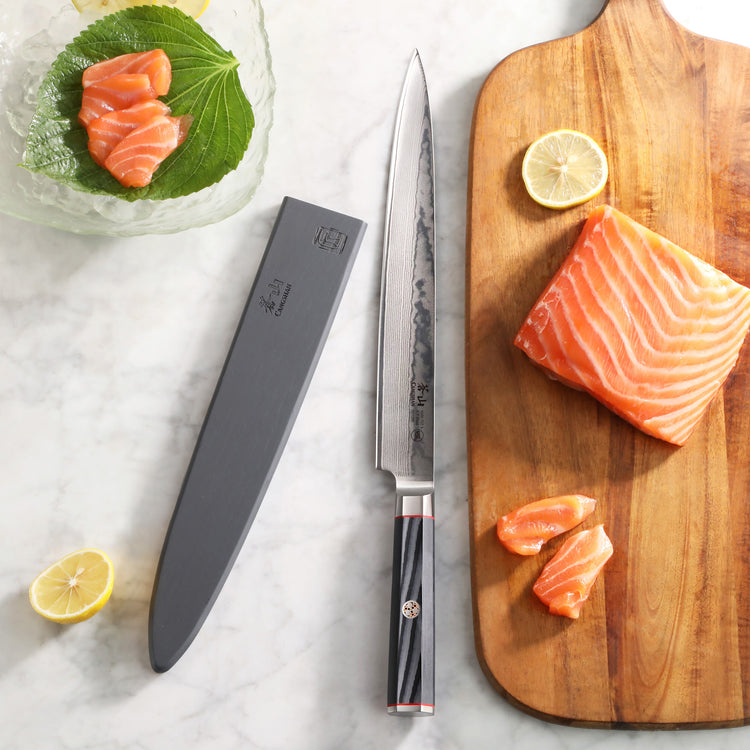 10-inch sashimi knife with black handle and sheath, next to sliced salmon and lemon on wooden board and plate.
