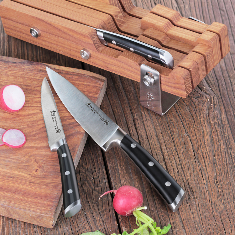 Two black-handled kitchen knives, one in a wooden knife block and two on a wooden surface with sliced radishes nearby.