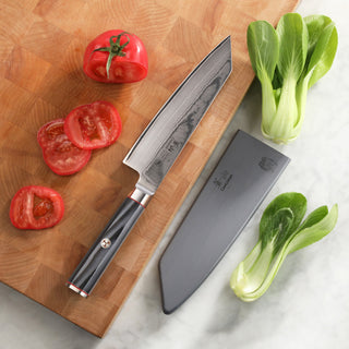 
                    
                      7-inch Kiritsuke knife with patterned blade and black handle, sheath, sliced tomato, and bok choy on cutting board and marble
                    
                  