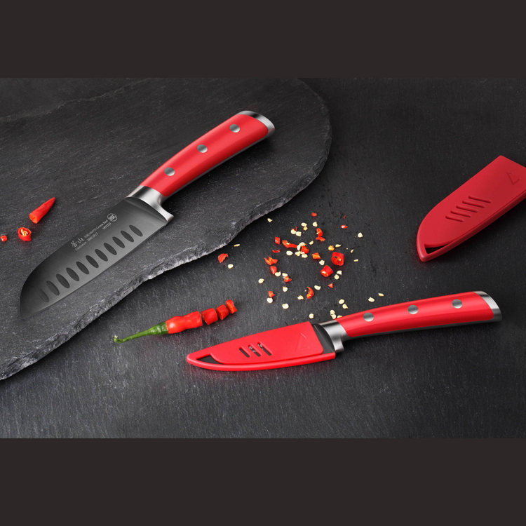 Two red-handled kitchen knives on a black surface with sliced and whole red chili peppers.