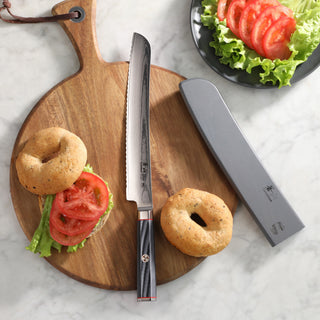 
                    
                      9-inch serrated bread knife with sheath on wooden cutting board, next to bagels and sliced tomatoes with lettuce.
                    
                  