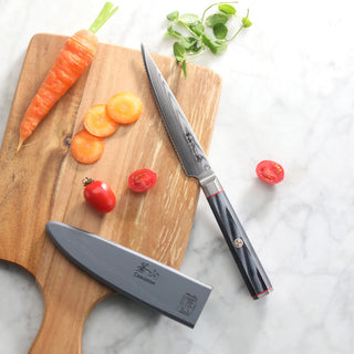 
                    
                      Serrated utility knife with sheath on wooden cutting board next to sliced carrot and cherry tomatoes.
                    
                  