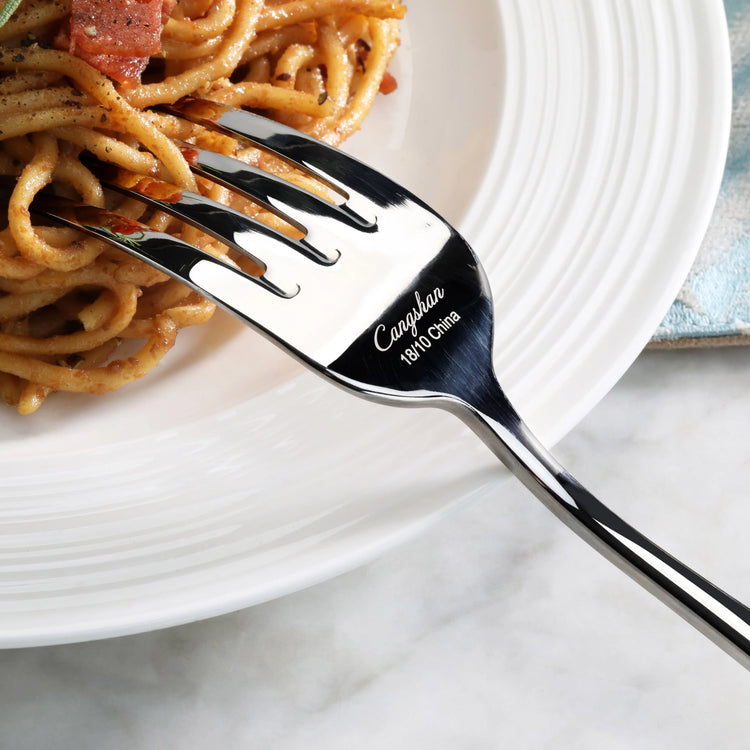 Serving fork with mirror finish holding spaghetti on a white ridged plate.