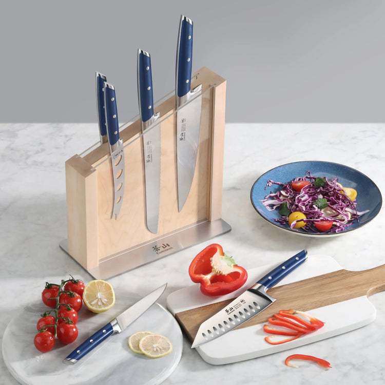 Seven-piece knife set with blue handles in a wooden block, displayed with sliced red bell pepper, cherry tomatoes, lemon, and