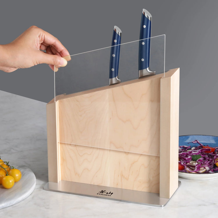 Wooden knife block with blue-handled knives and a clear protective shield being lifted by a hand.