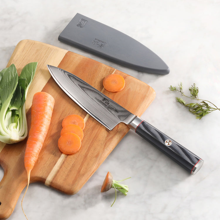 6-inch chef's knife with Damascus steel blade and sheath on cutting board with sliced carrot and bok choy.